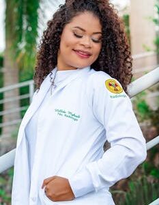 Radiology professional with curly hair smiling in a white coat outdoors.